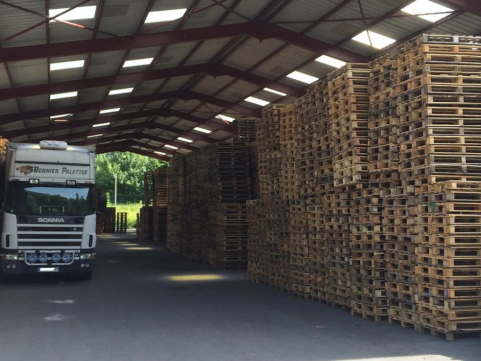 Entrepôt de Bernier Palettes avec un stock important de palettes en bois et un camion de livraison prêt à partir.