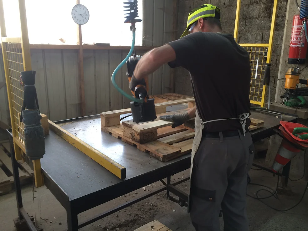 Ouvrier assemblant une palette en bois standard recyclée dans un atelier à Chambéry.